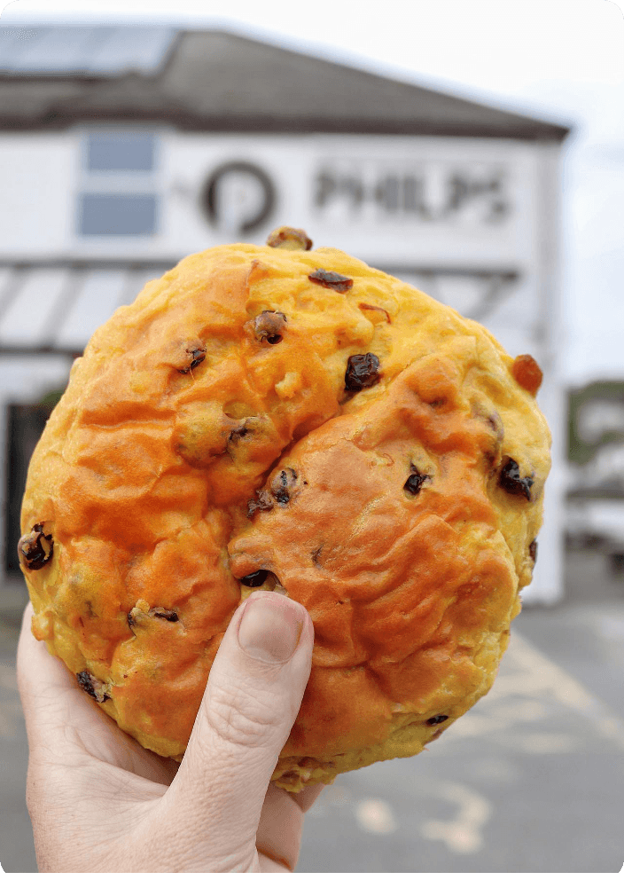 Hand holding a Cornish saffron bun outside the Philps bakery
